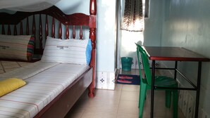 A single bed with a wooden frame, a green chair, a small table, and a window with patterned curtains.
