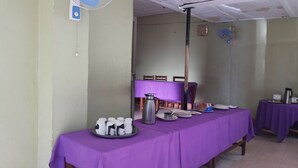 Un coin repas avec une nappe violette, une cafetière, des tasses et des assiettes.