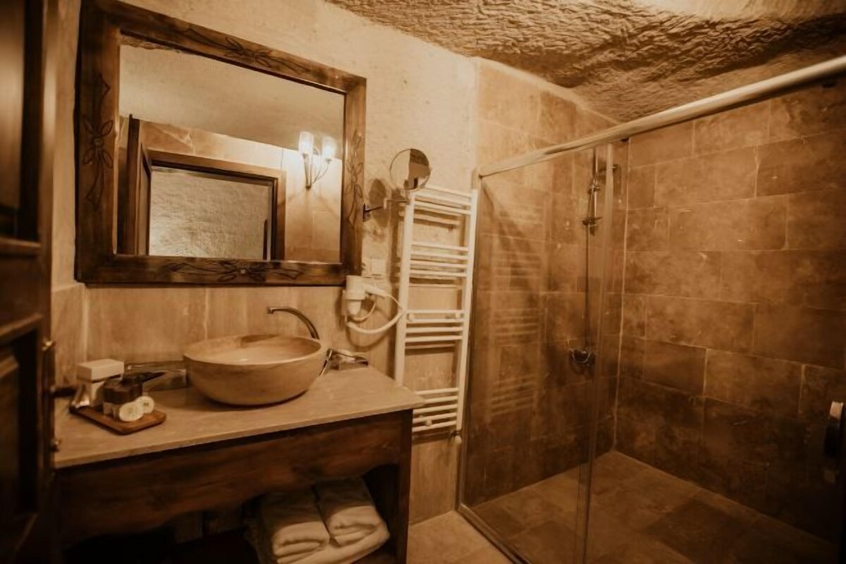 A bathroom with a wooden vanity, a round sink, a mirror, a towel rack, and a shower enclosure.
