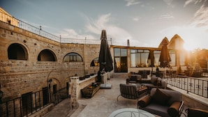Terraço no telhado com paredes de pedra, mesas ao ar livre e guarda-sóis.