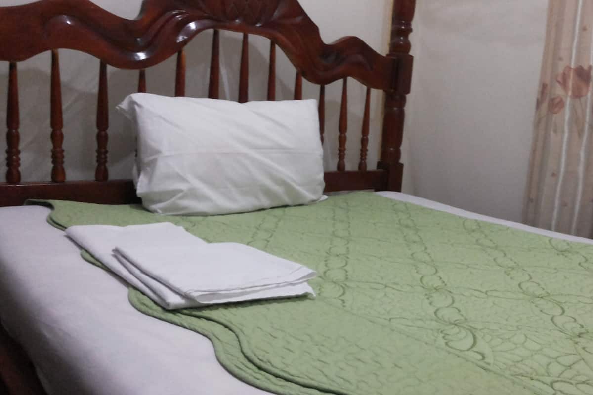 A bed with a wooden headboard, a green quilt, and a white pillow.