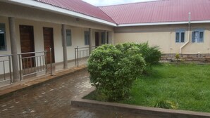 A building with a covered walkway, a small garden, and a brick pathway. - Dubai Resort Hotel (Adjumani)