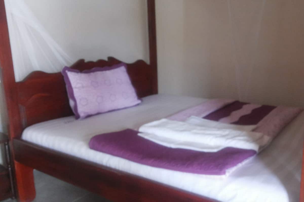 A bed with a wooden frame, white bedding, and a purple blanket.