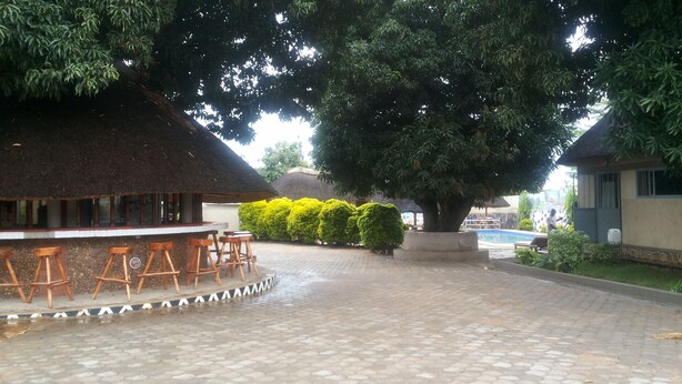 A bar area with stools, a thatched roof, and a paved walkway. - Dubai Resort Hotel (Adjumani)