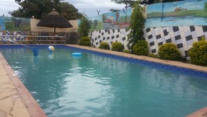 A swimming pool with a checkered tile border, a thatched umbrella, and a mural on the wall. - Dubai Resort Hotel (Adjumani)