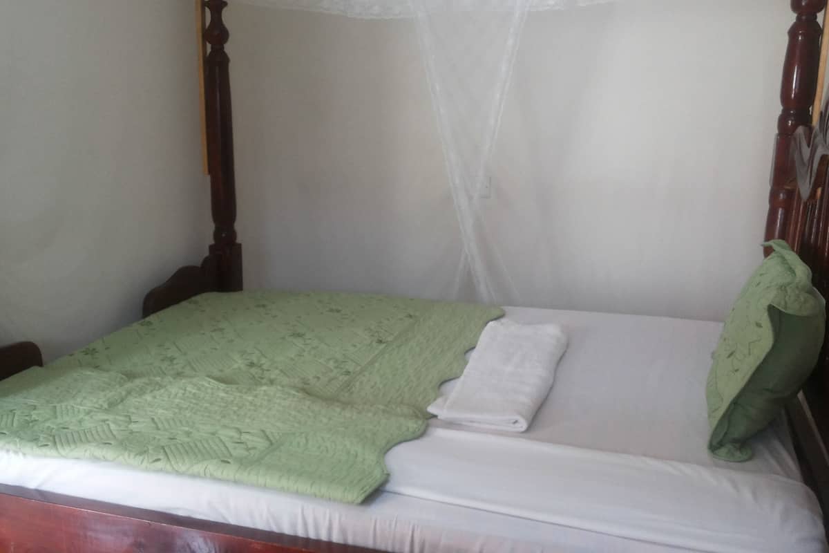A single bed with a green blanket and a white pillow in a room with a wooden headboard and a white canopy.