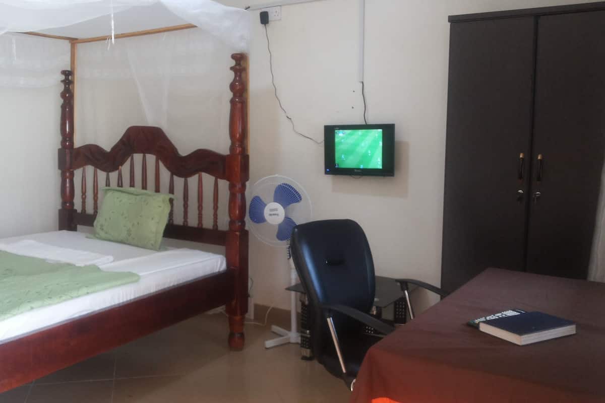 A bedroom with a four-poster bed, a desk with a chair, a television, and a wardrobe.