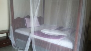 A bed with a mosquito net, a wooden headboard, and two pillows. - Dubai Resort Hotel (Adjumani)