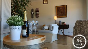 A modern living room with a sofa, a coffee table with a bottle of wine and glasses, a potted plant, and decorative wall art.