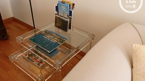 A glass-top coffee table with magazines and a book, a sofa with a patterned cushion, and a wall-mounted magazine rack.