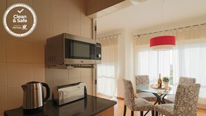 A modern kitchen with a microwave, toaster, and kettle on the counter. There is a dining area with a glass table and chairs.