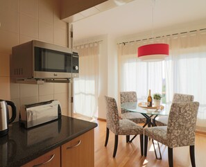 Eine moderne Küche mit Mikrowelle, Toaster und Wasserkocher auf der Arbeitsplatte. Ein Essbereich mit Glastisch und Stühlen ist ebenfalls vorhanden.