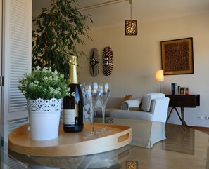 Ein modernes Wohnzimmer mit einer Couch, einem Couchtisch mit einer Weinflasche und Gläsern, einer Topfpflanze und Wanddekoration.