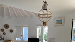 A modern living room with a wooden dining table, white chairs, a flat-screen TV, and a ceiling fan.