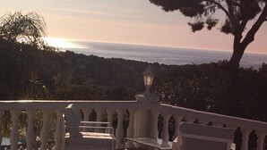 A balcony with a view of the ocean, a lamp, and a bench.
