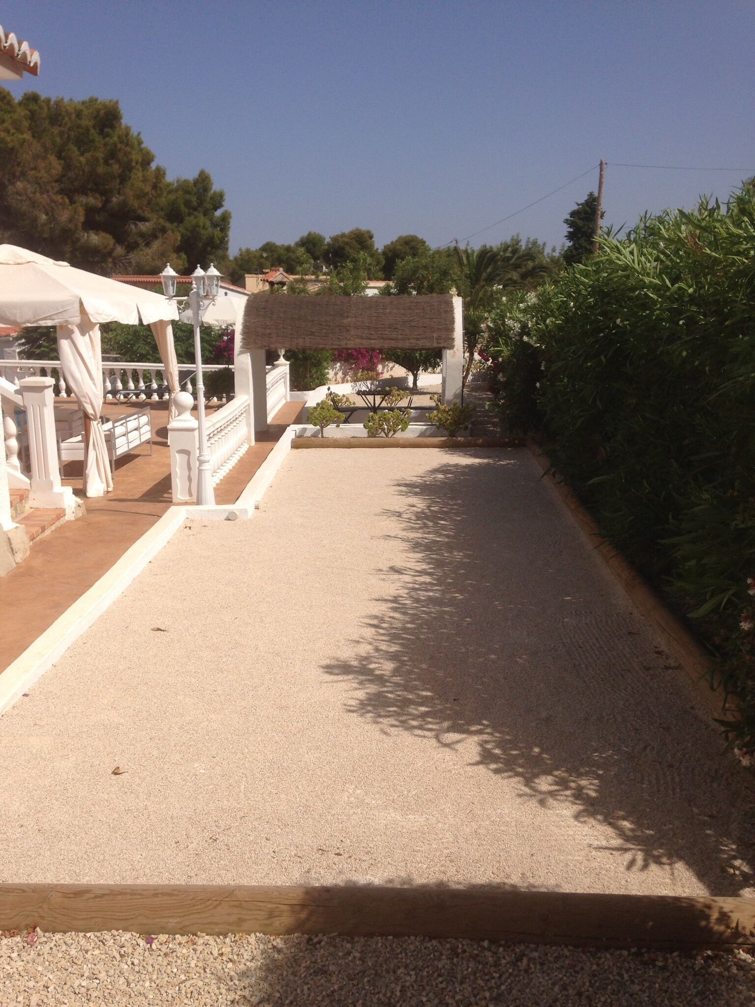Un chemin pavé mène à un belvédère blanc surmonté d’une pergola, le tout étant entouré de verdure et surplombé par un ciel dégagé.