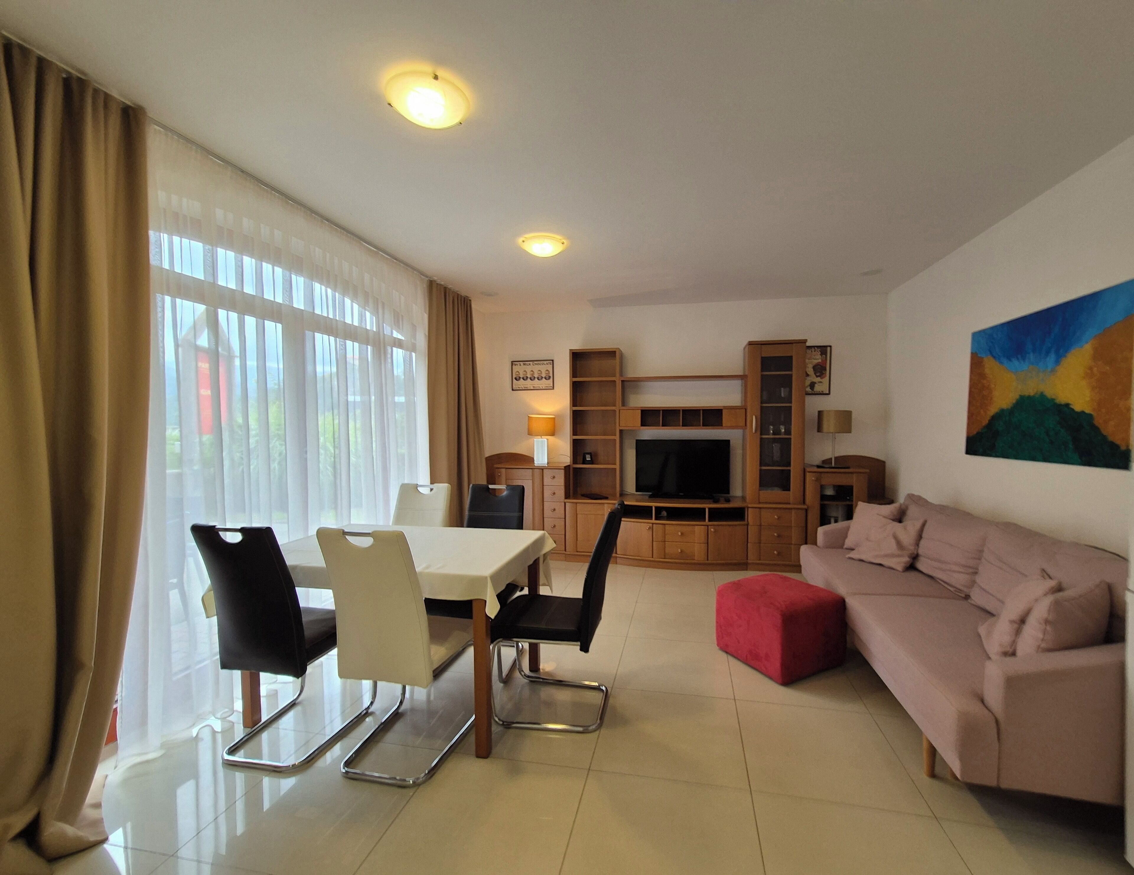 A modern living room with a dining area, a sofa, a TV, and a painting on the wall.