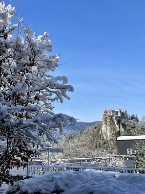 A snow-covered landscape with a castle on a cliff, a sign reading "Hotel", and a building with a sign that reads "HUB". - Aparthotel Gaja (Bled)