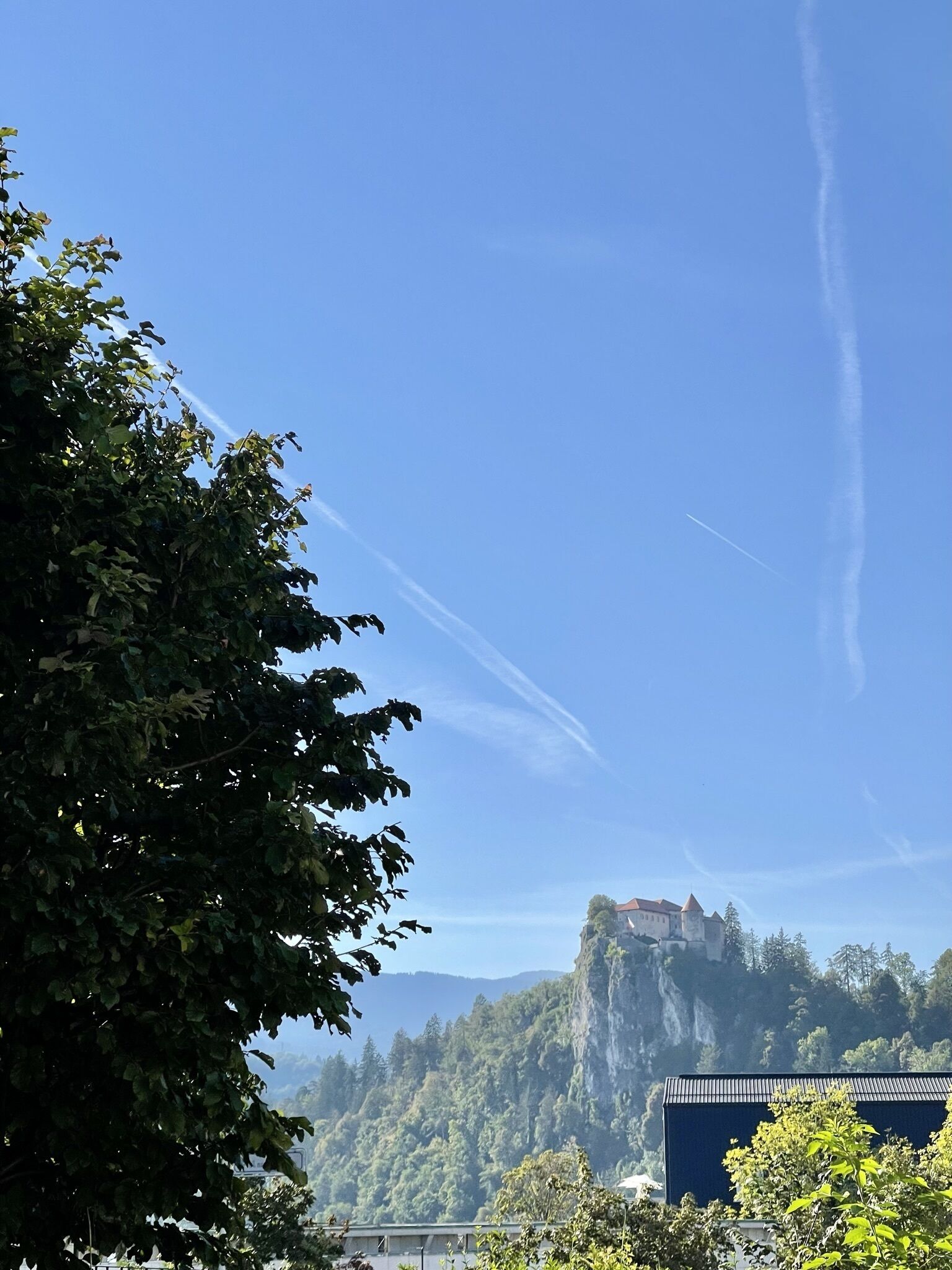 A castle on a cliff with a clear sky and contrails.