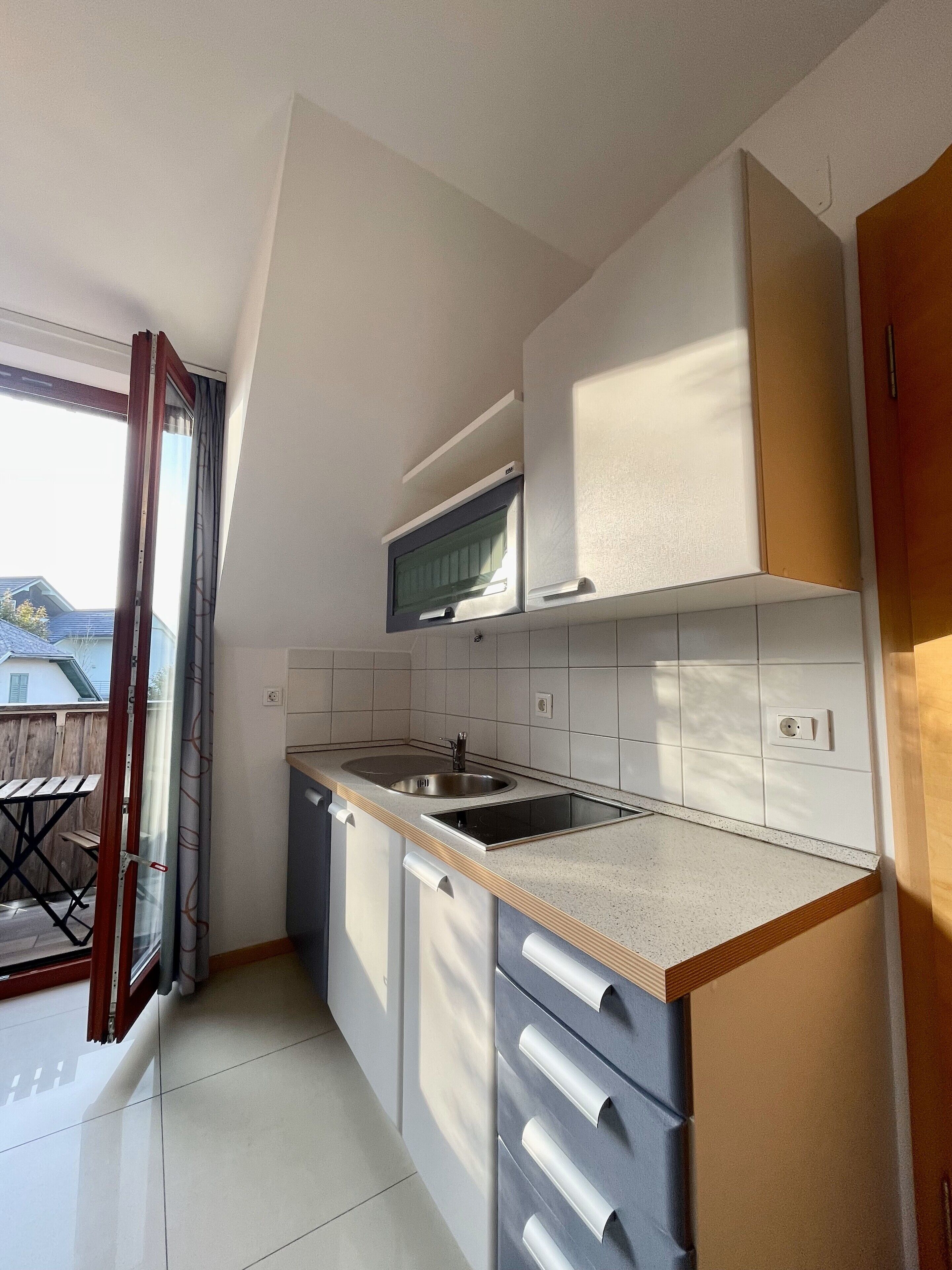Una cucina moderna con forno a incasso, microonde e lavandino. Una porta scorrevole dà accesso a un patio.