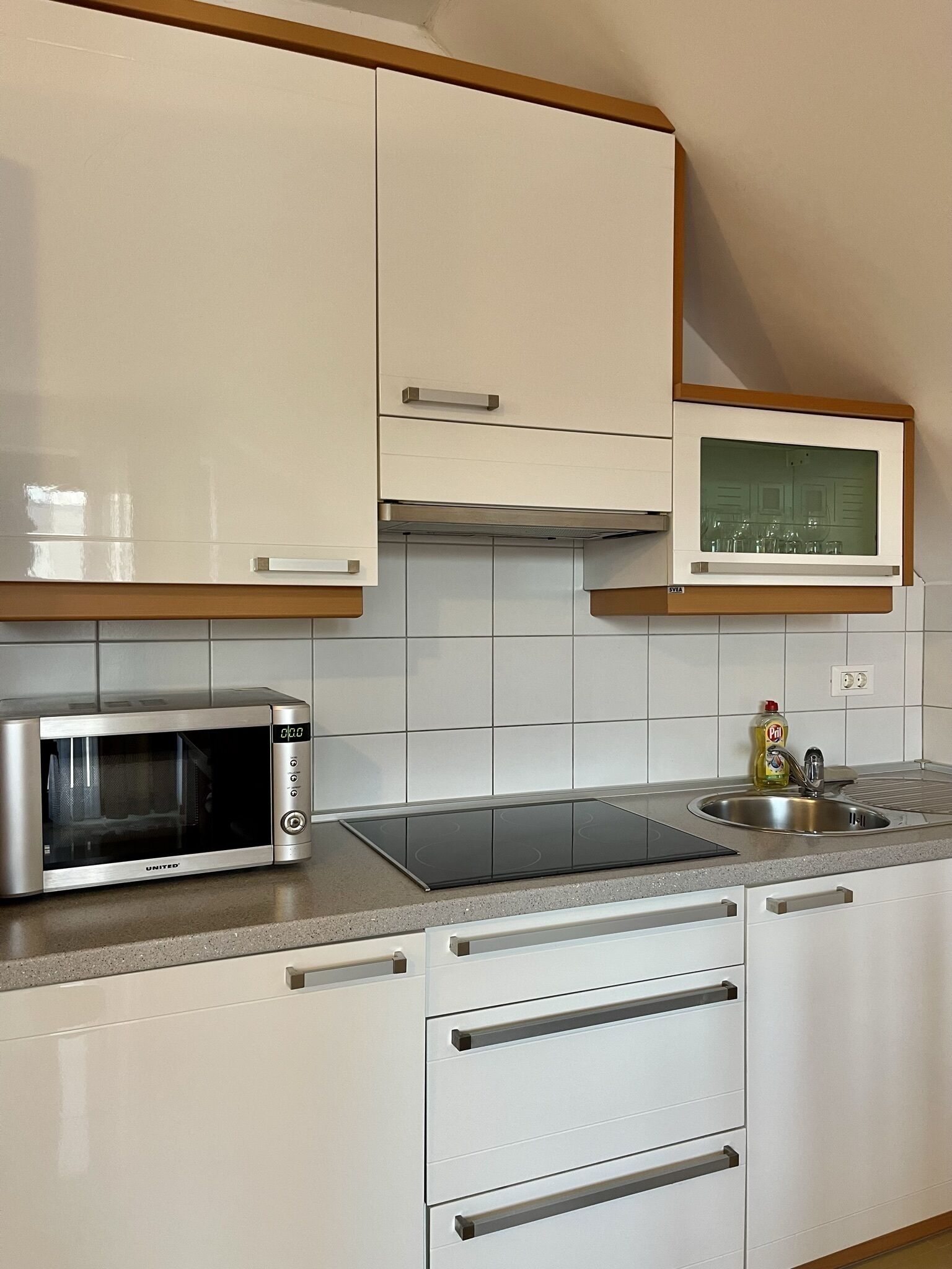Une cuisine compacte avec des meubles blancs, un four à micro-ondes encastré, une cuisinière et une petite fenêtre au-dessus de l’évier.