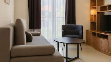 A modern living room with a sofa, a chair, a small table, a TV stand, and a large window with curtains.