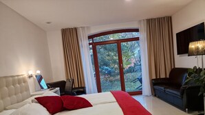 Una habitación de hotel con cama, escritorio con computadora, sofá de cuero y un ventanal con cortinas.