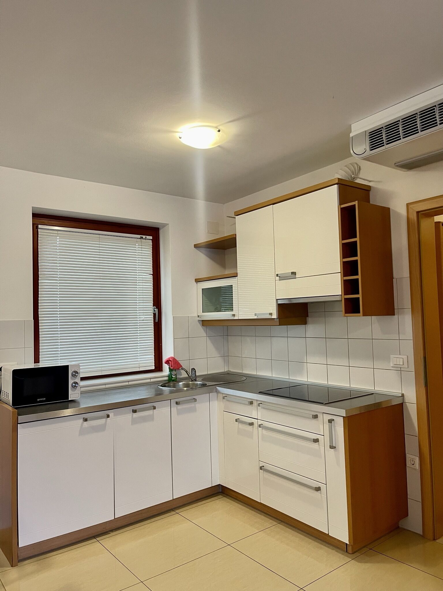 A compact kitchen with white cabinets, a microwave, a sink, and a window with blinds.