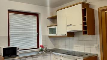 A compact kitchen with white cabinets, a microwave, a sink, and a window with blinds.