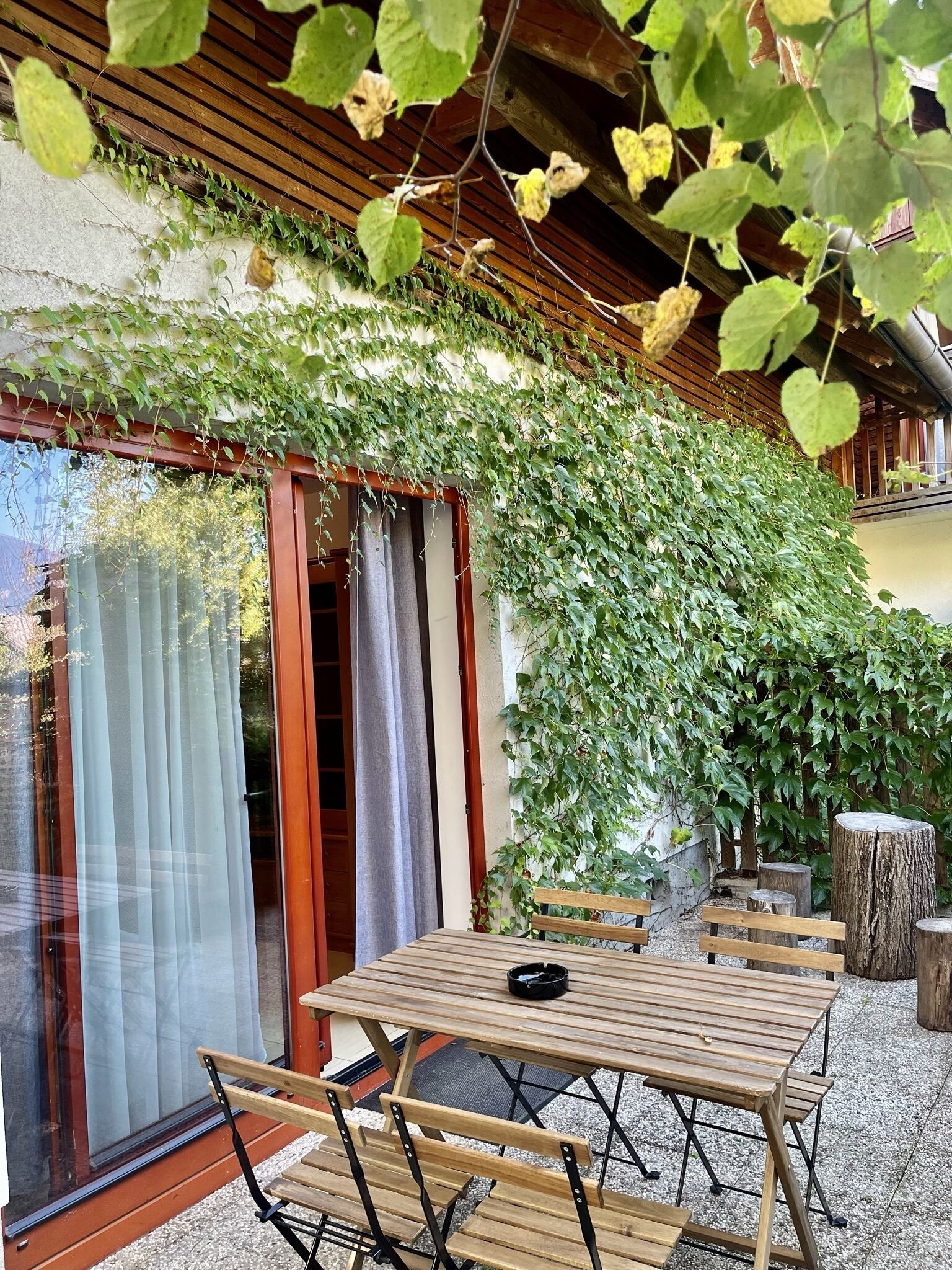 Un conjunto de mesa y sillas de madera en un patio de grava, con un caballete de madera y un banco.