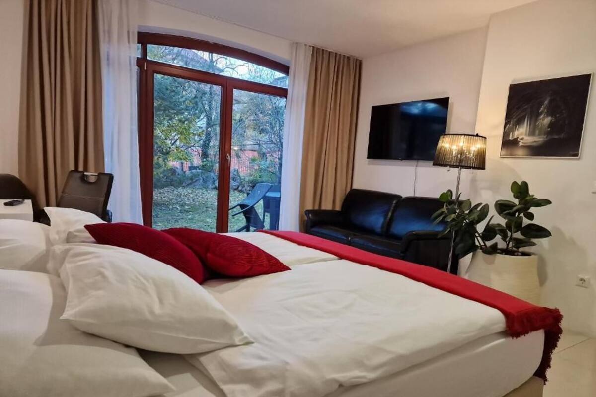 A hotel room with a large bed, a sofa, a TV, and a window with curtains.