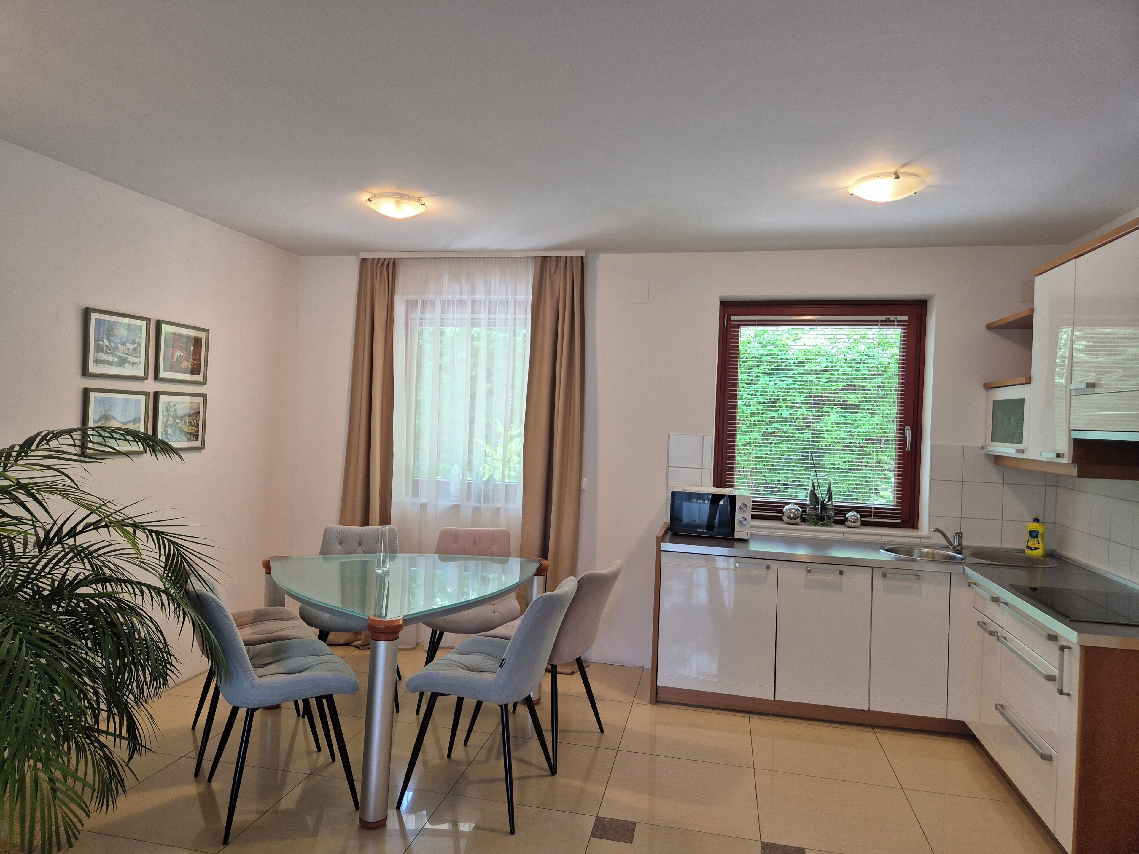 Una cucina moderna con un tavolo da pranzo in vetro, mobili bianchi e una finestra con persiane.