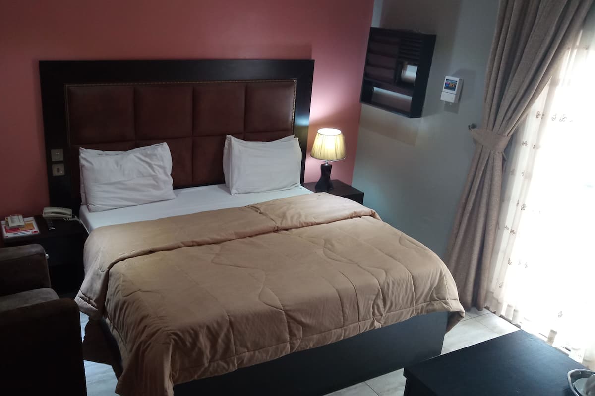 A hotel room with a bed, bedside tables, a lamp, and a window with curtains.