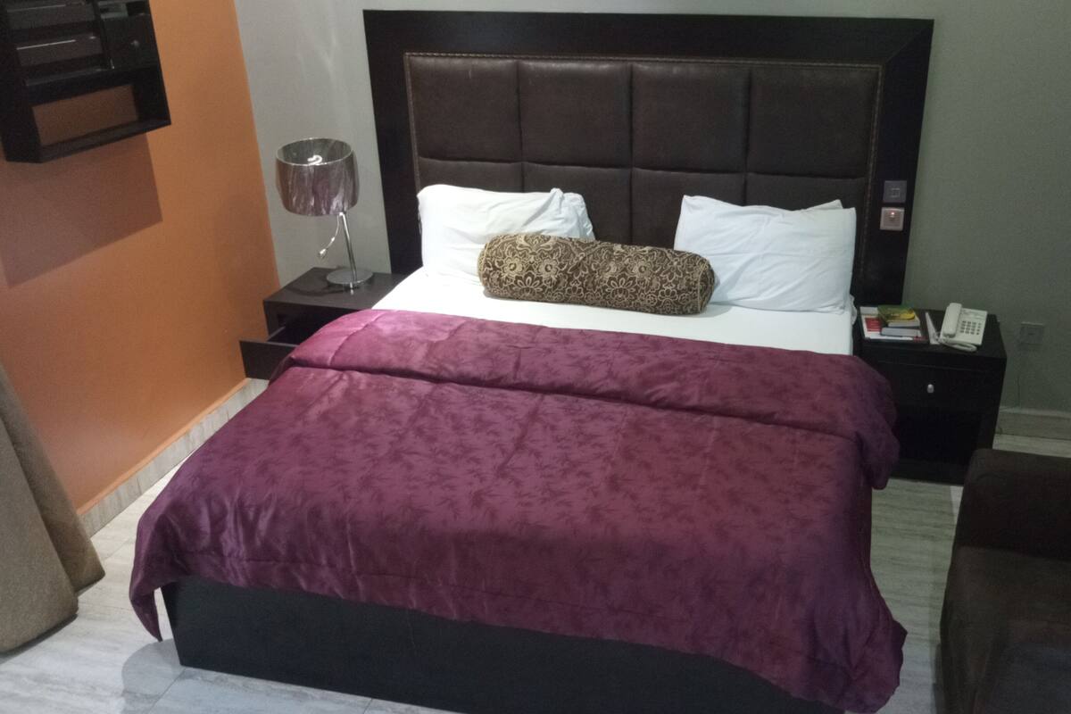 A neatly made bed with a dark headboard, a purple bedspread, and a patterned pillow.