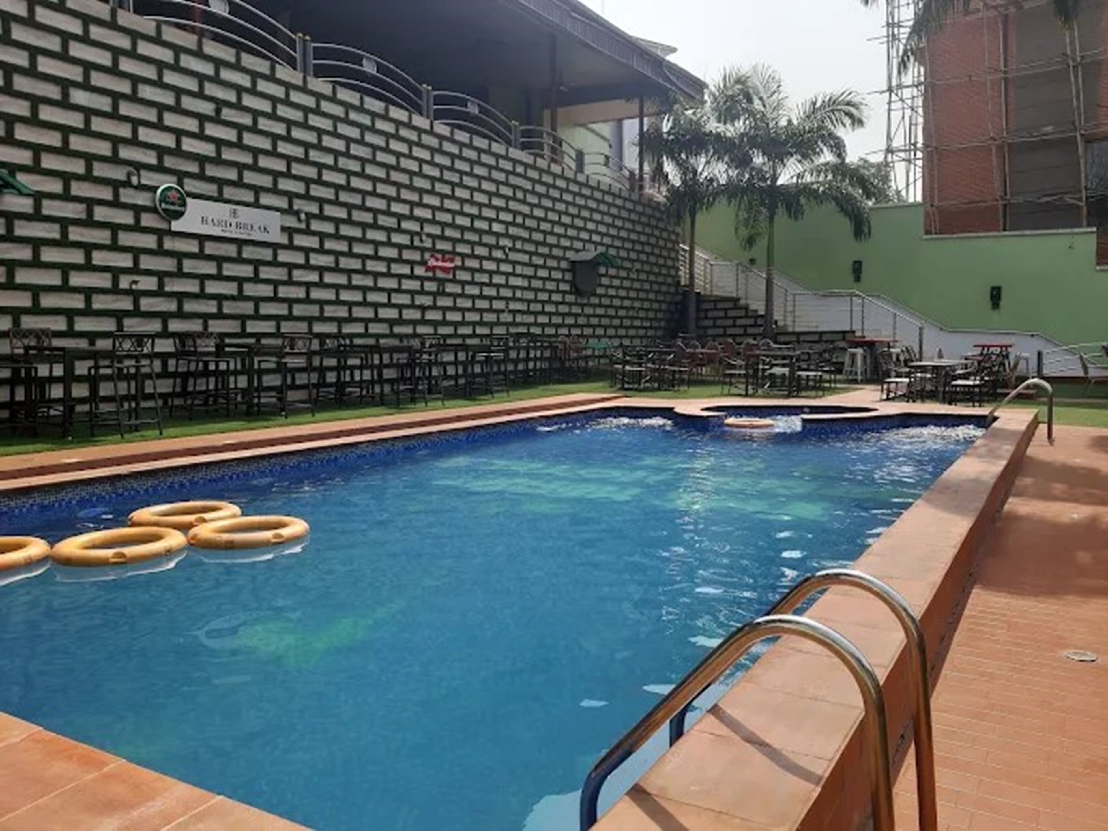 Una piscina con pared de ladrillo y una placa, rodeada de mobiliario exterior y palmeras.
