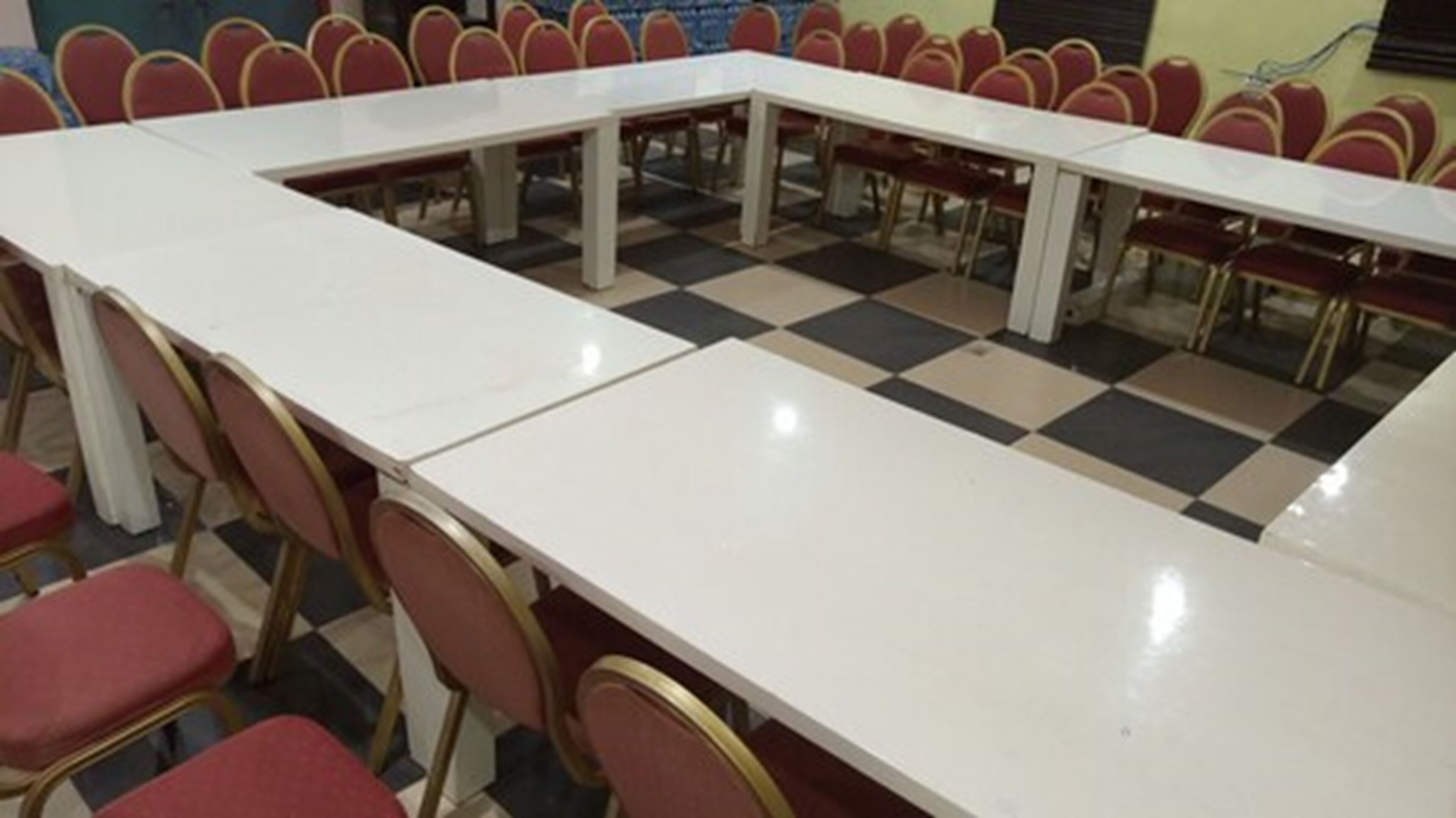 A conference room with a long rectangular table surrounded by red chairs.