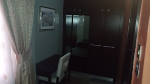 A room with a bed, a chair, a small table, and a wardrobe. - Hard Break Hotel and Suite (Enugu)