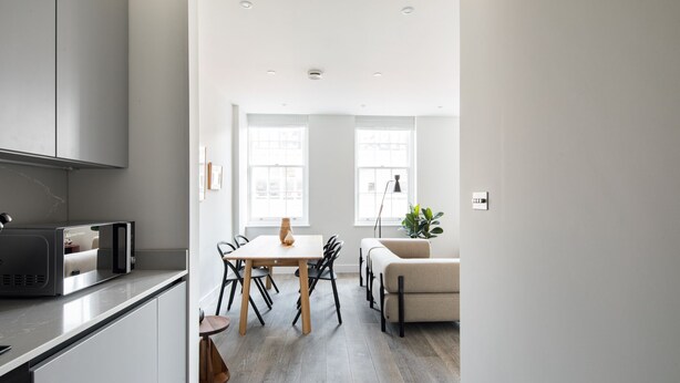 A modern kitchen with a built-in microwave, a dining area with a wooden table and chairs, and a light-colored sofa in a bright living space.
