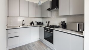 A modern kitchen with white cabinetry, a black stove, a microwave, and a coffee maker.