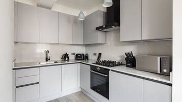 A modern kitchen with white cabinetry, a black stove, a microwave, and a coffee maker.