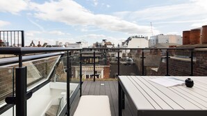 A rooftop terrace with a glass balustrade, wooden tables, and a view of the cityscape. - Spacious Leicester Sq 3BR Penthouse (London)