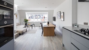 A modern kitchen with a central island, a dining area with a sofa and table, and a large window providing natural light. - Spacious Leicester Sq 3BR Penthouse (London)