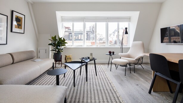A modern living room with a sofa, a dining table, a chair, and a large window with a city view. - Spacious Leicester Sq 3BR Penthouse (London)