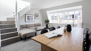 A modern living room with a wooden dining table, a sofa, and a staircase. - Spacious Leicester Sq 3BR Penthouse (London)