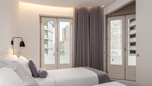 Hotellihuone, jossa on kaksi sänkyä, suuri ikkuna ja näkymä ulkona oleviin rakennuksiin.