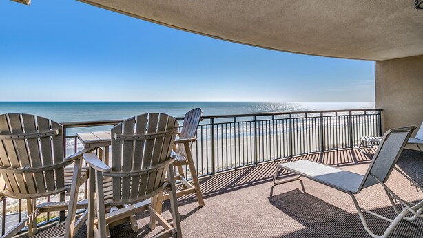 A balcony with Adirondack chairs and a table overlooking a beach. - 🌊🌞Lazy River + Indoor/Outdoor Pools | Oceanfront | South Wind 1101 (Myrtle Beach)