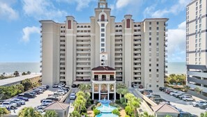 A multi-story hotel with a central tower, a parking lot, and a pool area. - 🌊🌞Lazy River + Indoor/Outdoor Pools | Oceanfront | South Wind 1101 (Myrtle Beach)