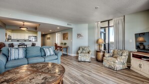 A spacious living room with a blue sofa, two armchairs, a coffee table, and a TV. - 🌊🌞Lazy River + Indoor/Outdoor Pools | Oceanfront | South Wind 1101 (Myrtle Beach)
