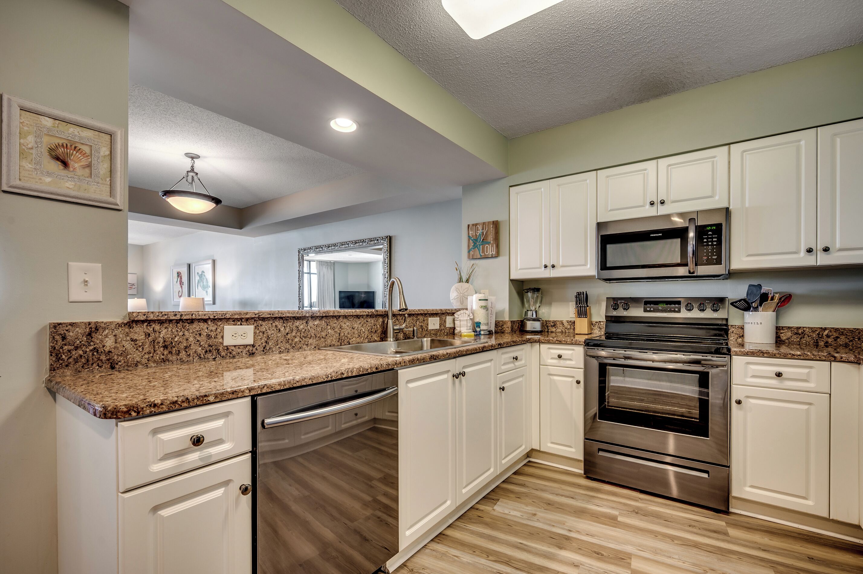 A modern kitchen with white cabinets, granite countertops, stainless steel appliances, and a wooden floor.