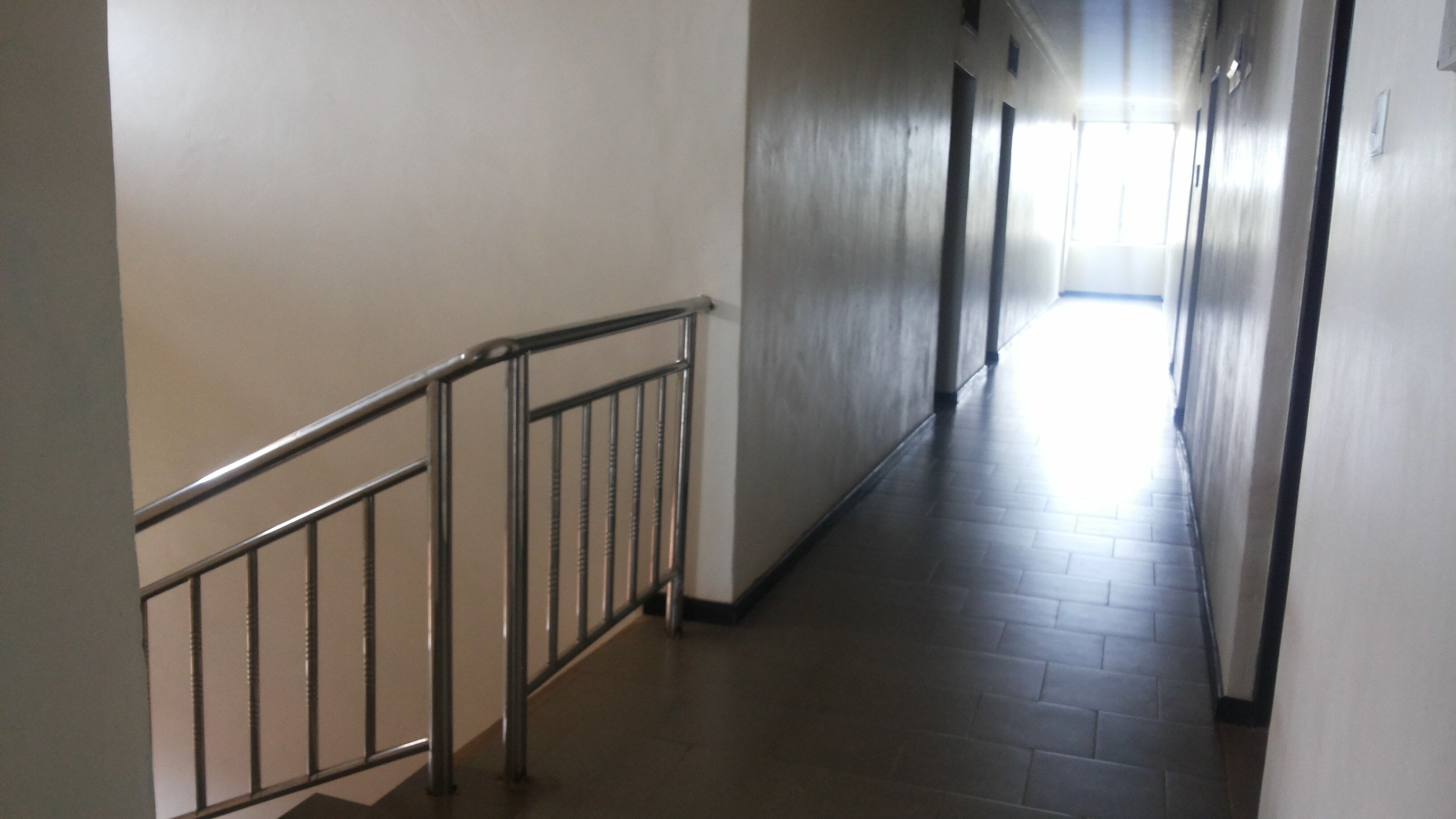 A long, narrow hallway with a metal railing on one side and a tiled floor.